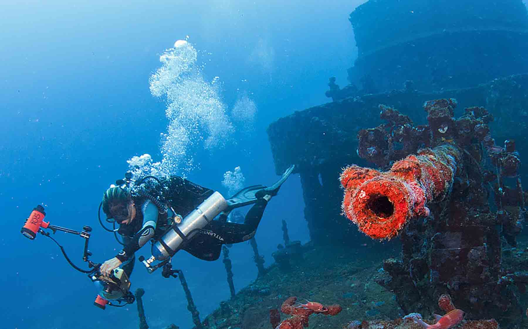 Aqui, um fotógrafo subaquática leva a câmera com na caixa-estanque com domo e dois flashes presos a braços laterais
